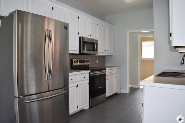 4802 David Dr, Texarkana, TX 75503 - kitchen with stainless steel appliances, a sink, white cabinets, dark tile patterned flooring, and decorative backsplash