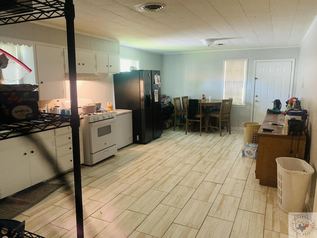 kitchen with white cabinets, black refrigerator with ice dispenser, a wealth of natural light, and white gas range