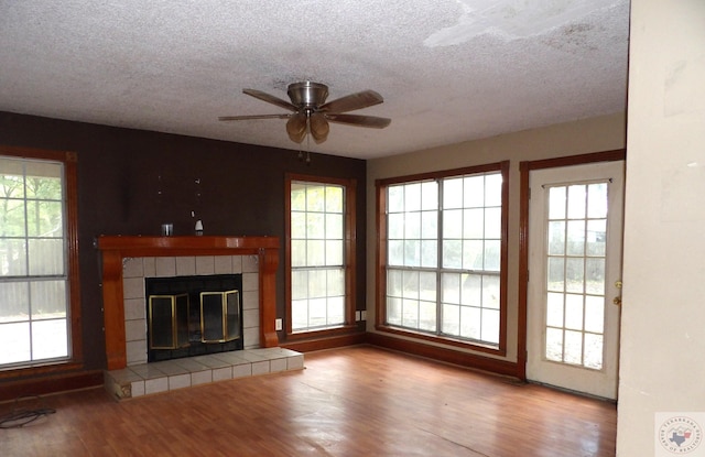 unfurnished living room featuring a tile fireplace, light hardwood / wood-style floors, a textured ceiling, and ceiling fan