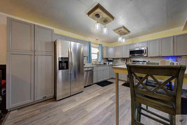 kitchen featuring appliances with stainless steel finishes, light hardwood / wood-style flooring, hanging light fixtures, gray cabinetry, and decorative backsplash