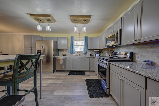 kitchen featuring appliances with stainless steel finishes, gray cabinetry, tasteful backsplash, and decorative light fixtures