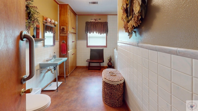 bathroom featuring ornamental molding, toilet, and tile walls