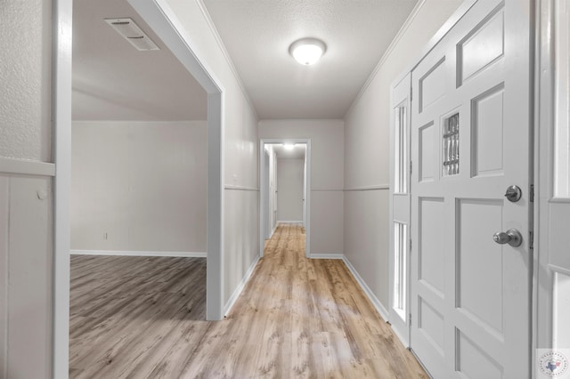 hallway with a textured ceiling, light hardwood / wood-style flooring, and ornamental molding