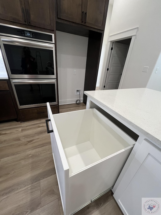 kitchen with hardwood / wood-style flooring, stainless steel double oven, and dark brown cabinets