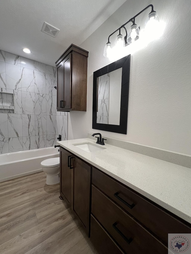 full bathroom with wood-type flooring, tiled shower / bath combo, toilet, a textured ceiling, and vanity