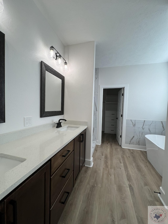 bathroom with hardwood / wood-style floors, a textured ceiling, tile walls, a washtub, and vanity