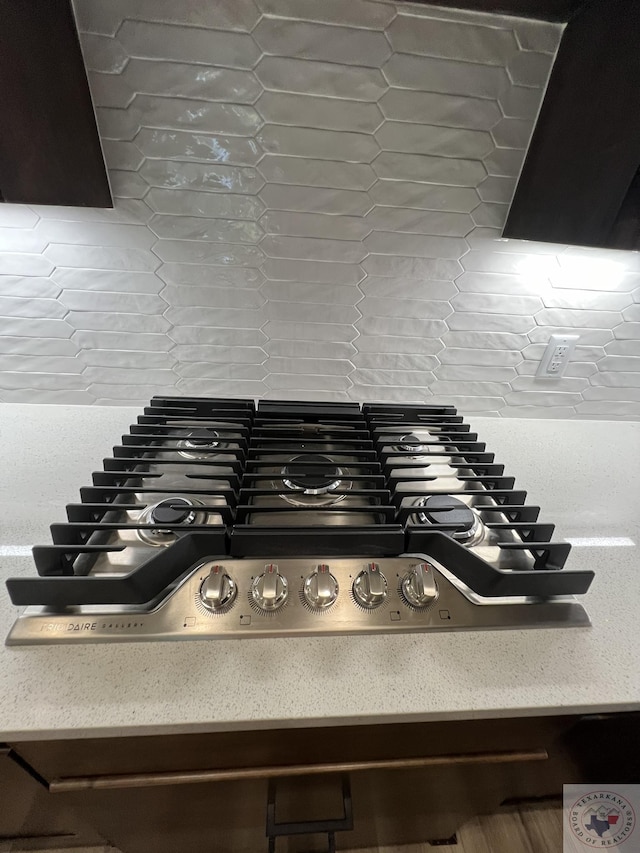 room details featuring range hood, tasteful backsplash, and gas stovetop