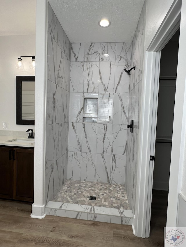 bathroom featuring hardwood / wood-style floors, tiled shower, and vanity