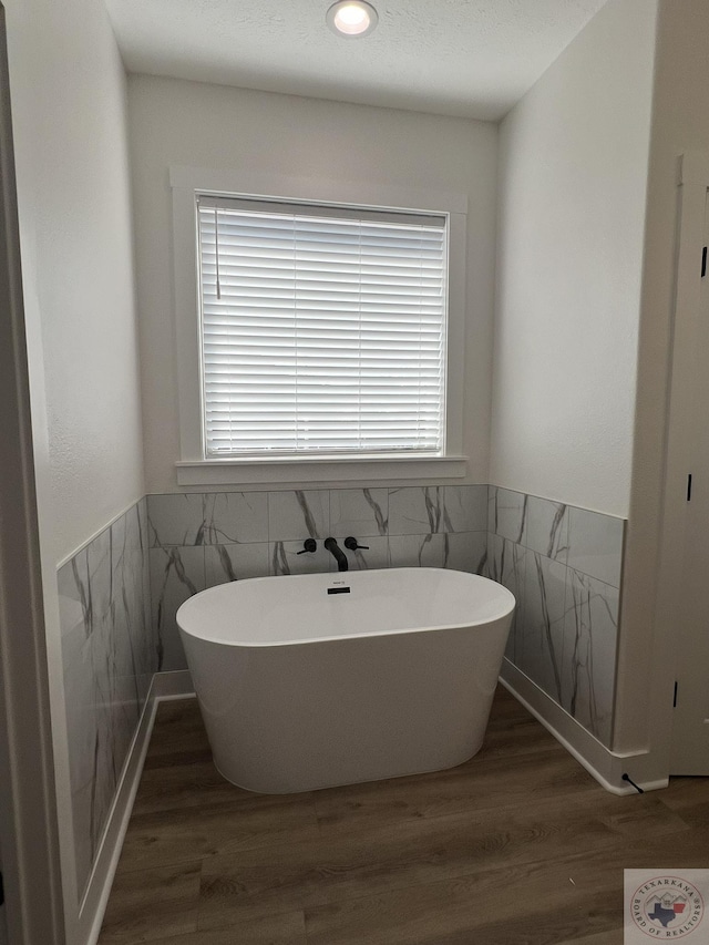 bathroom with hardwood / wood-style floors, plenty of natural light, a bath, and tile walls