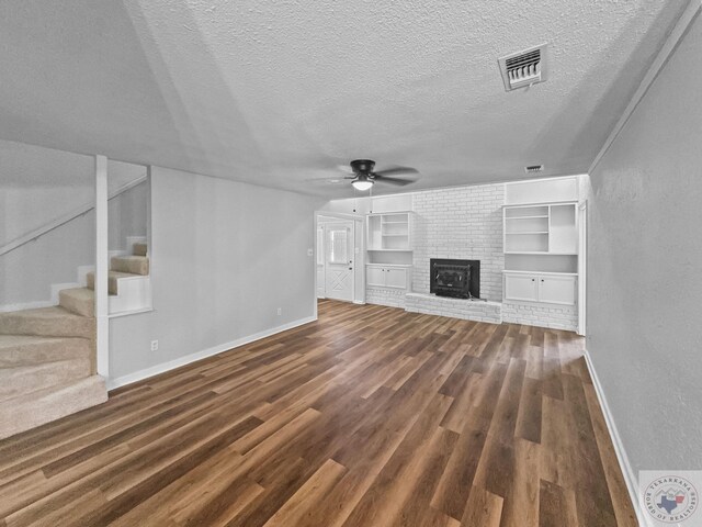 unfurnished living room with a brick fireplace, dark wood-type flooring, a textured ceiling, and ceiling fan