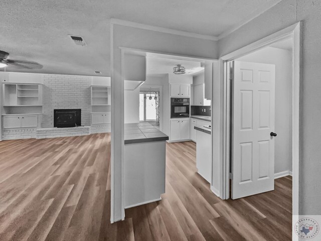 kitchen with ceiling fan, white cabinetry, a brick fireplace, a textured ceiling, and black oven