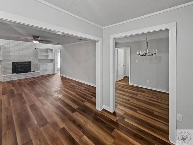 unfurnished living room featuring built in features, dark wood-type flooring, a brick fireplace, ceiling fan with notable chandelier, and a textured ceiling