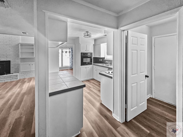 kitchen with white cabinets, a fireplace, a textured ceiling, dark hardwood / wood-style floors, and black oven