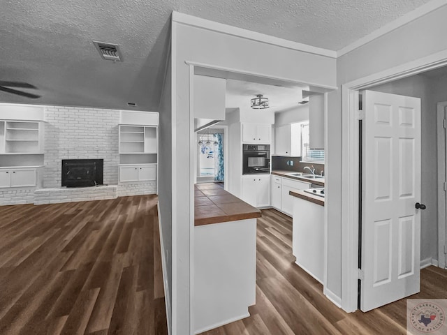 kitchen with a textured ceiling, a fireplace, white cabinetry, dark wood-type flooring, and black oven