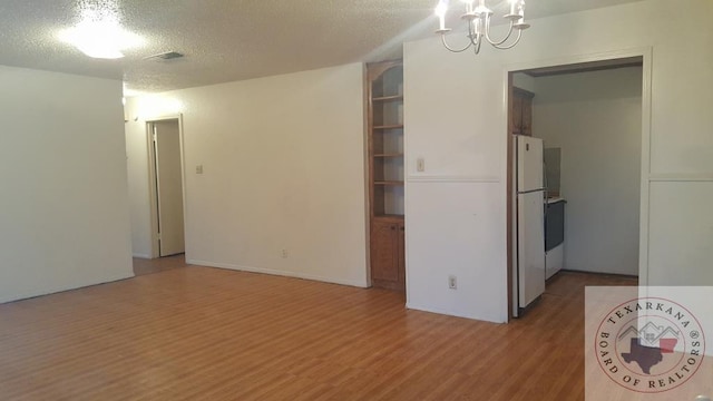 interior space with hardwood / wood-style floors, a chandelier, a textured ceiling, and white refrigerator