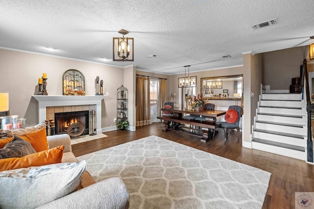 living room featuring dark wood-type flooring, a tile fireplace, crown molding, and a chandelier