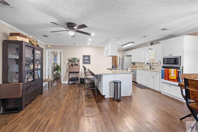 kitchen featuring light stone countertops, white cabinetry, backsplash, stainless steel appliances, and a breakfast bar area