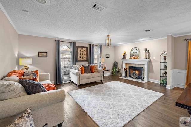 living room with dark wood-type flooring, a textured ceiling, a tile fireplace, and ornamental molding