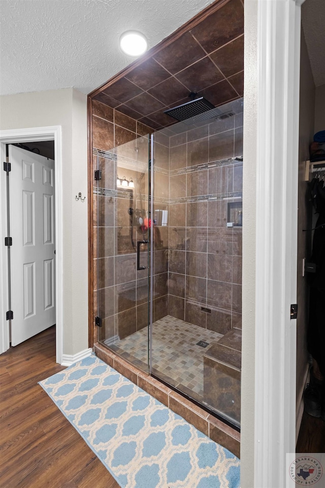 bathroom with hardwood / wood-style flooring, a textured ceiling, and a shower with shower door