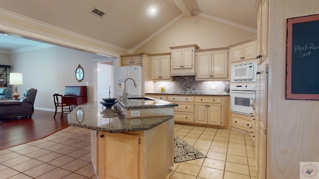 kitchen featuring sink, tasteful backsplash, white appliances, vaulted ceiling with beams, and a center island with sink