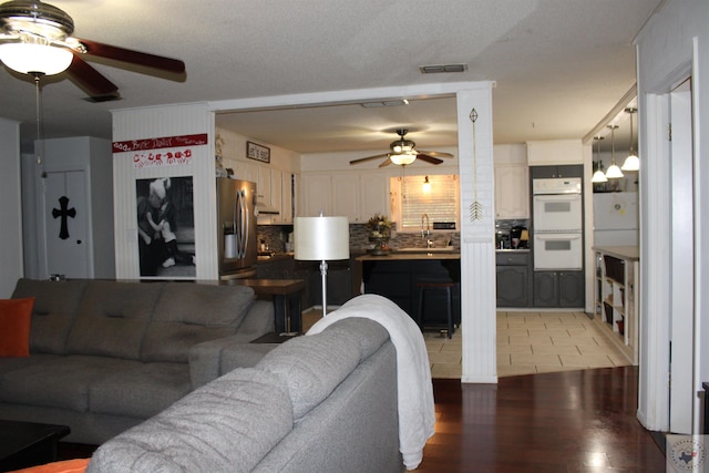 living room with sink, ceiling fan, light hardwood / wood-style floors, and a textured ceiling