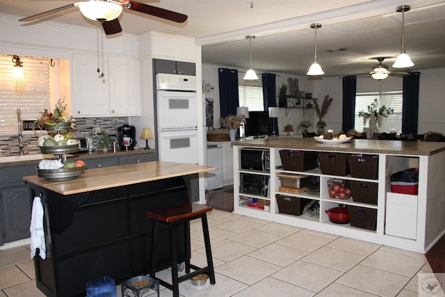 kitchen with white cabinetry, light tile patterned flooring, white appliances, a kitchen island, and decorative backsplash