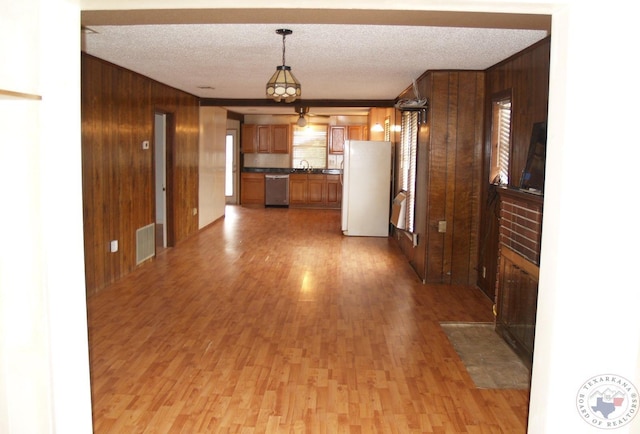 kitchen featuring dishwasher, hanging light fixtures, white refrigerator, a textured ceiling, and wooden walls