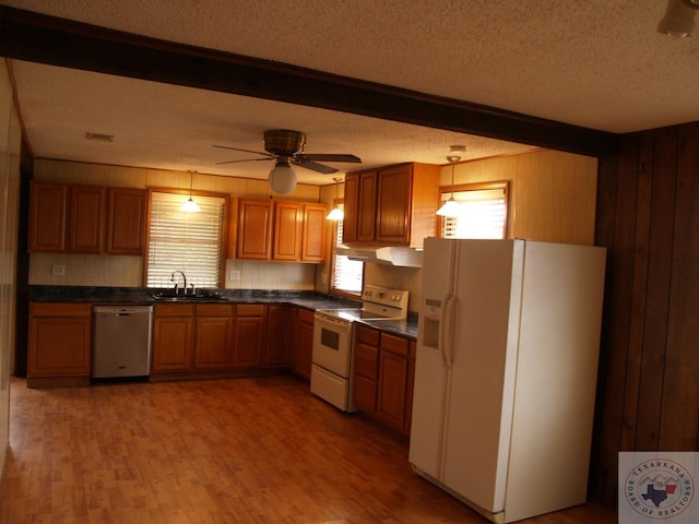 kitchen featuring decorative light fixtures, sink, white appliances, a textured ceiling, and wood walls