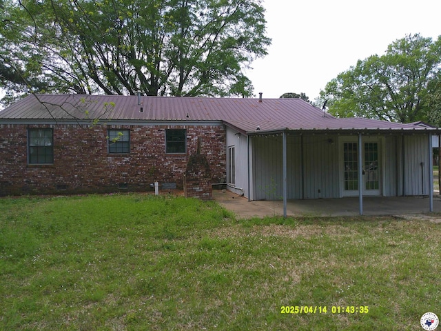 rear view of house with metal roof, brick siding, a yard, crawl space, and a patio