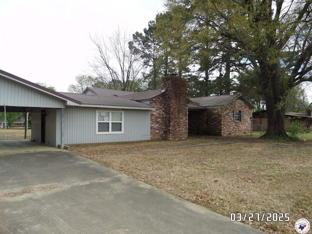 view of side of property with concrete driveway, an attached carport, a chimney, and metal roof