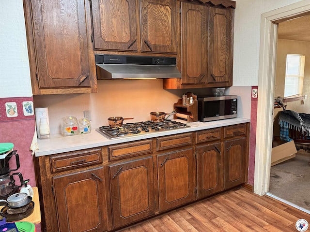 kitchen featuring light countertops, light wood-style flooring, under cabinet range hood, and appliances with stainless steel finishes