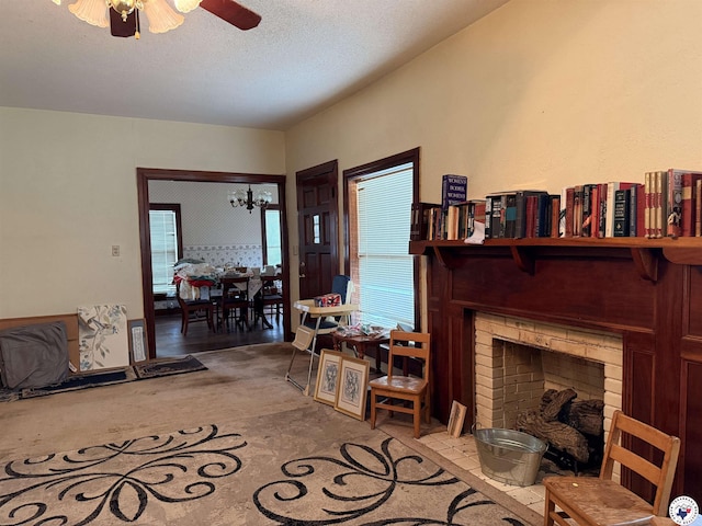 carpeted living area with ceiling fan with notable chandelier, a fireplace, and a textured ceiling
