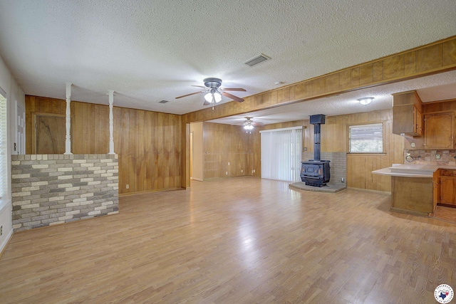 814 Hawkins Ave, Wake Village, TX 75501 - unfurnished living room featuring a wood stove, wood walls, a textured ceiling, a ceiling fan, and light wood-type flooring