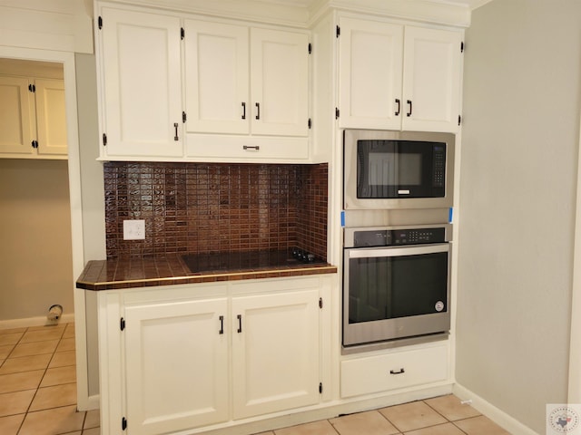 kitchen featuring oven, built in microwave, black electric stovetop, light tile patterned floors, and white cabinets