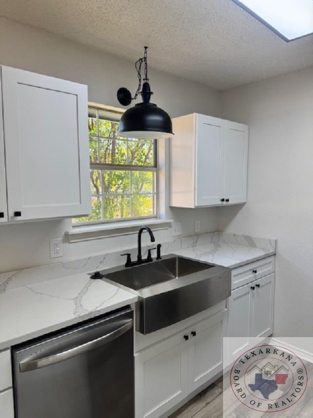 kitchen with stainless steel dishwasher, sink, white cabinetry, light stone counters, and a textured ceiling