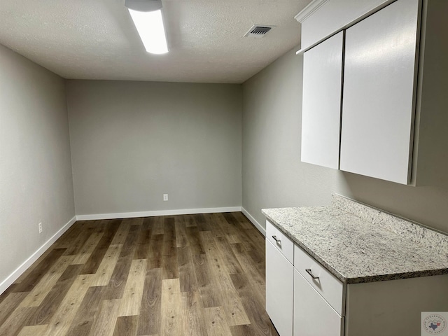 kitchen featuring a textured ceiling, light wood-type flooring, white cabinetry, and light stone countertops