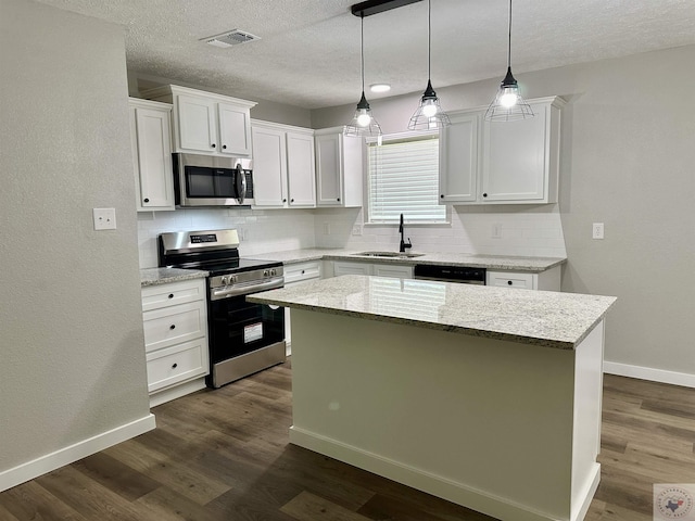 kitchen featuring appliances with stainless steel finishes, sink, white cabinetry, light stone countertops, and a center island