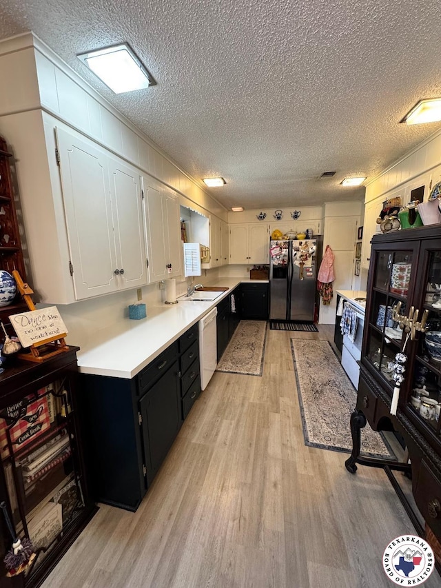 1509 W 40th St, Texarkana, TX 75503 - kitchen featuring white appliances, light wood-style floors, a textured ceiling, dark cabinetry, and light countertops