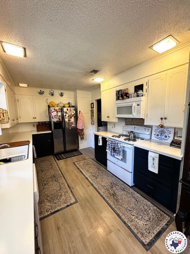 1509 W 40th St, Texarkana, TX 75503 - kitchen with white appliances, a textured ceiling, light wood finished floors, white cabinetry, and light countertops