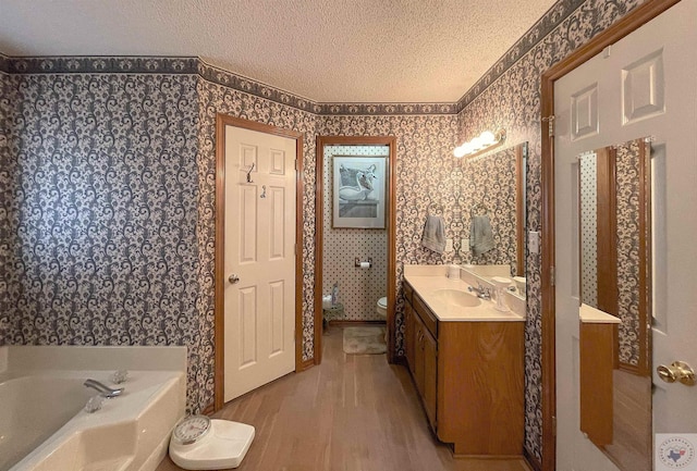 bathroom with toilet, hardwood / wood-style floors, a textured ceiling, vanity, and a bathing tub