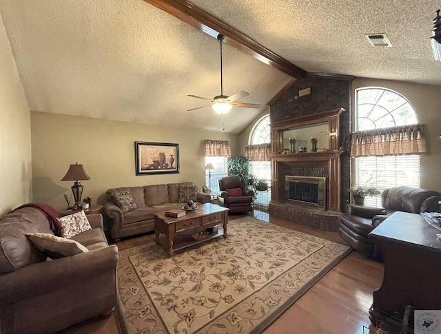 living room featuring wood-type flooring, lofted ceiling with beams, a brick fireplace, and plenty of natural light