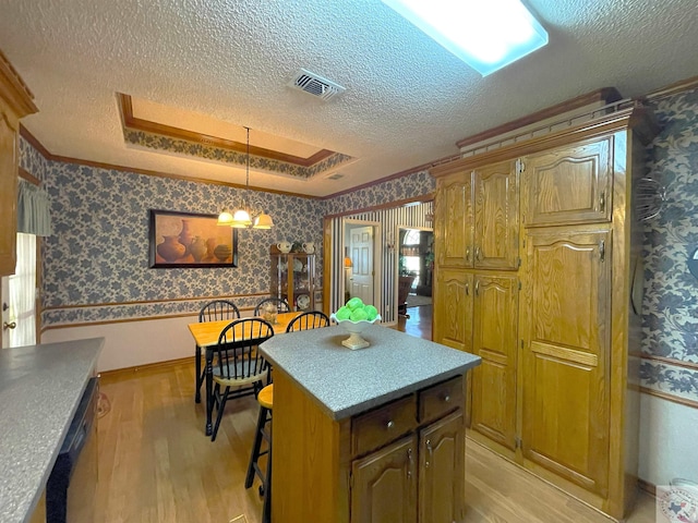 kitchen with decorative light fixtures, a raised ceiling, a kitchen island, and light hardwood / wood-style flooring