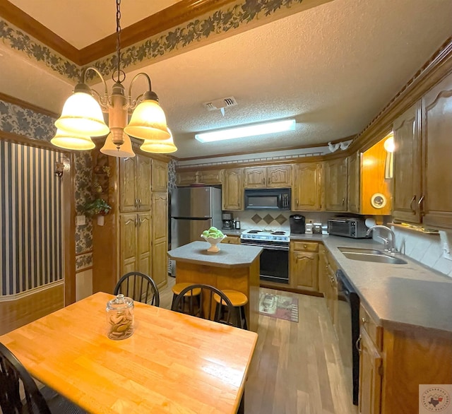 kitchen with a kitchen island, decorative light fixtures, sink, black appliances, and light wood-type flooring