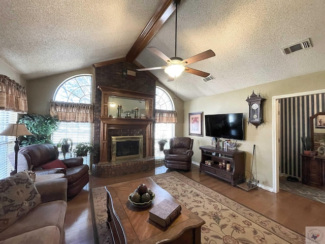 living room featuring ceiling fan, a fireplace, wood-type flooring, lofted ceiling with beams, and a textured ceiling