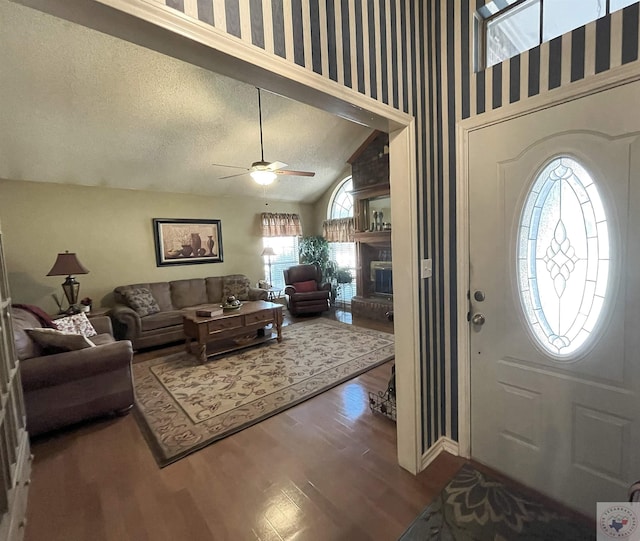 entrance foyer featuring lofted ceiling, ceiling fan, hardwood / wood-style floors, a fireplace, and a textured ceiling