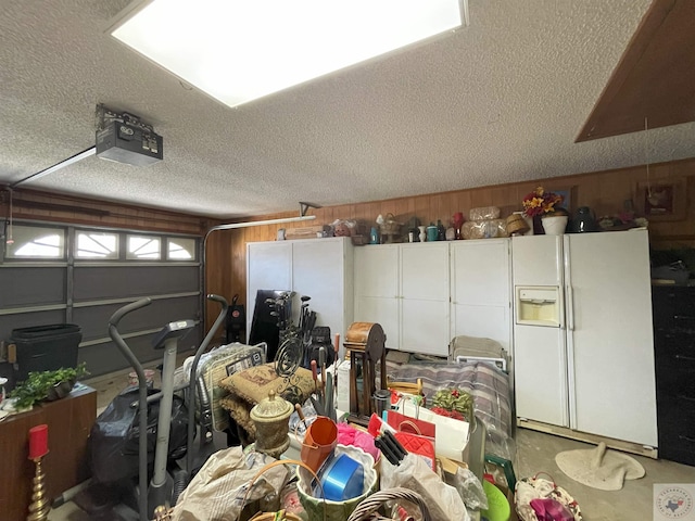 garage featuring wood walls, a garage door opener, and white fridge with ice dispenser