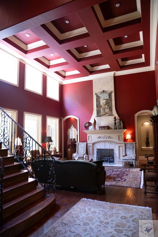 living room featuring wood-type flooring, crown molding, a fireplace, coffered ceiling, and beamed ceiling