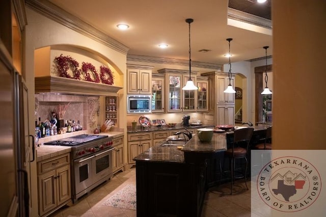 kitchen featuring pendant lighting, high quality appliances, sink, dark stone counters, and a center island with sink