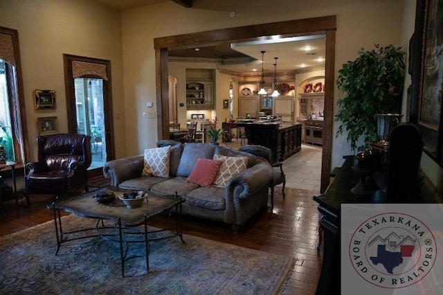 living room with wood-type flooring, beamed ceiling, ornamental molding, and a chandelier