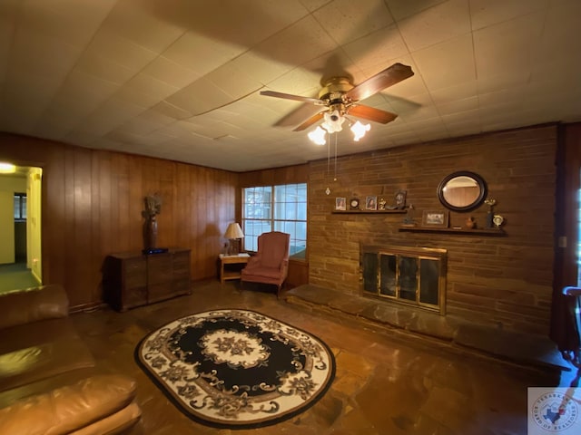 living room with ceiling fan, a stone fireplace, and wood walls